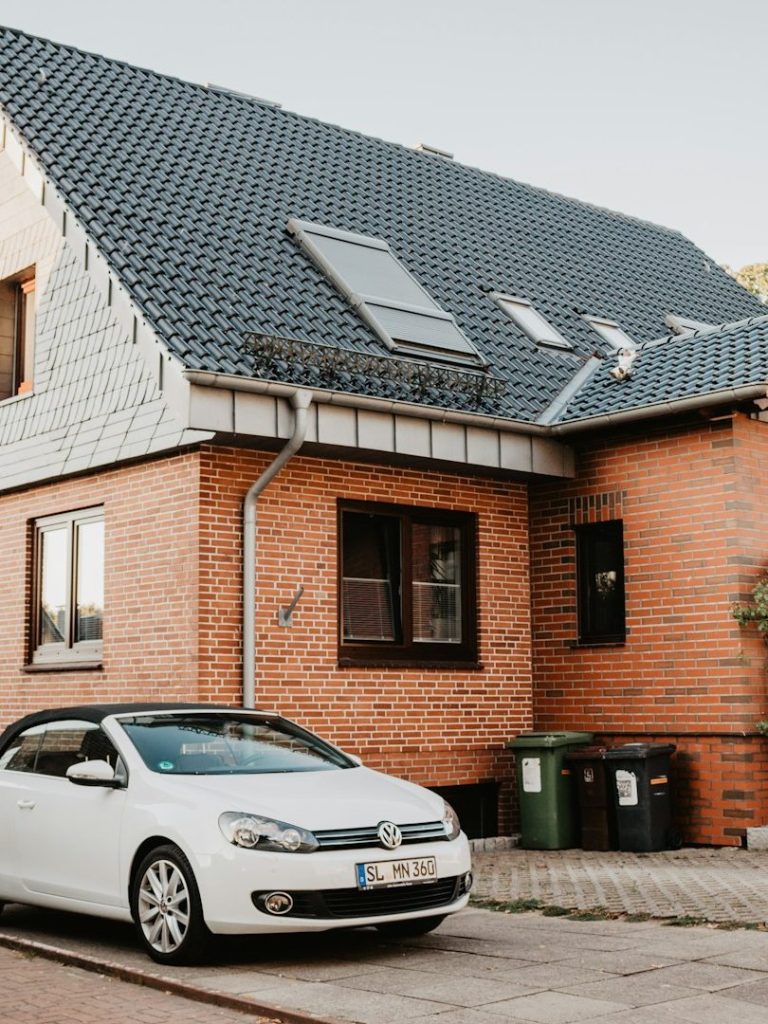Weißes Auto steht vor einem modernen, zweigeschossigen Ziegelhaus mit Dachfenstern.